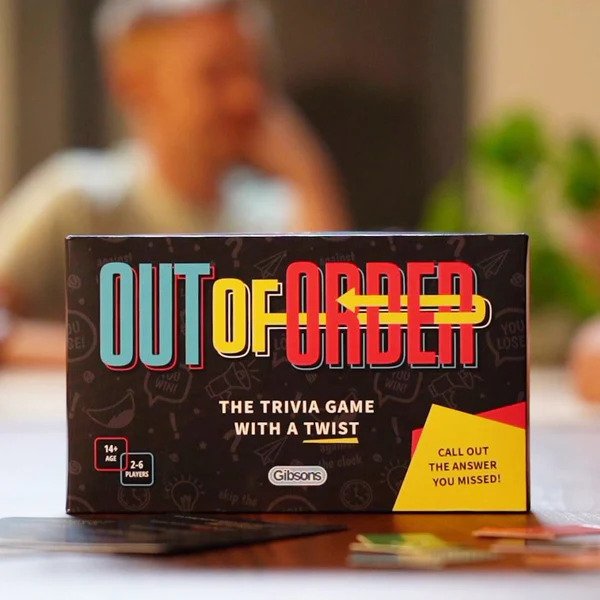 The Out of Order trivia card game box on a table surrounded by people playing.
