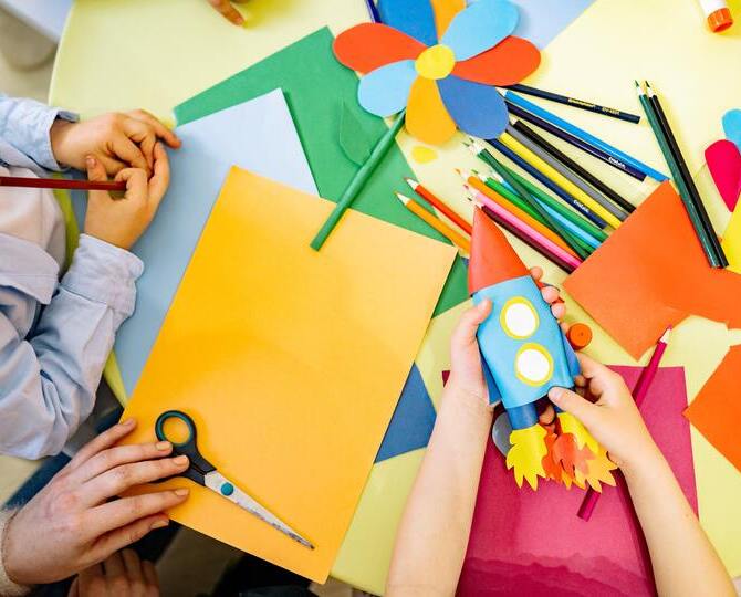 Children and an adult crafting using paper and drawing pencils.