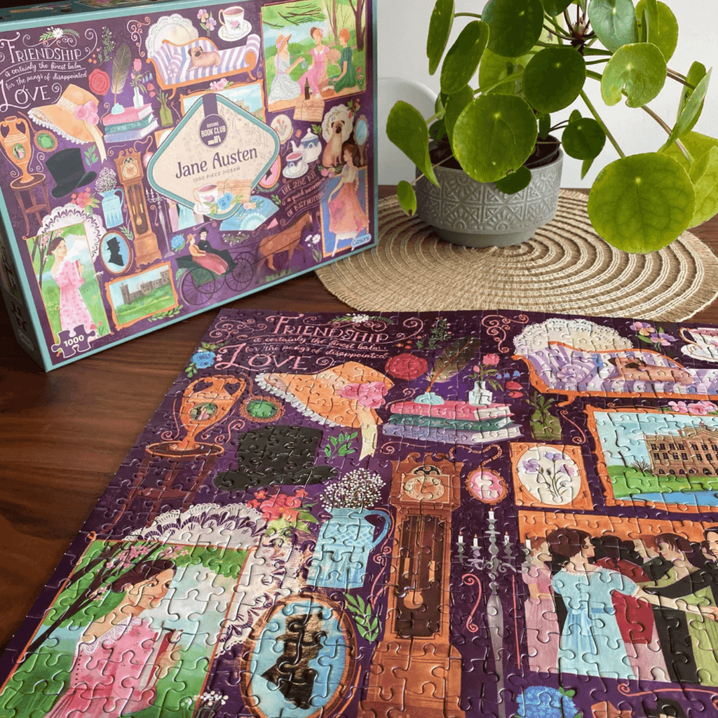 Jane Austen jigsaw puzzle on a wooden table with a plant next to it.