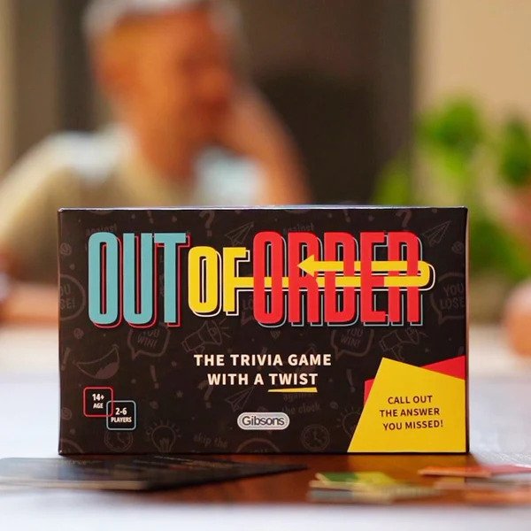 The Out of Order trivia card game box on a table surrounded by people playing. 