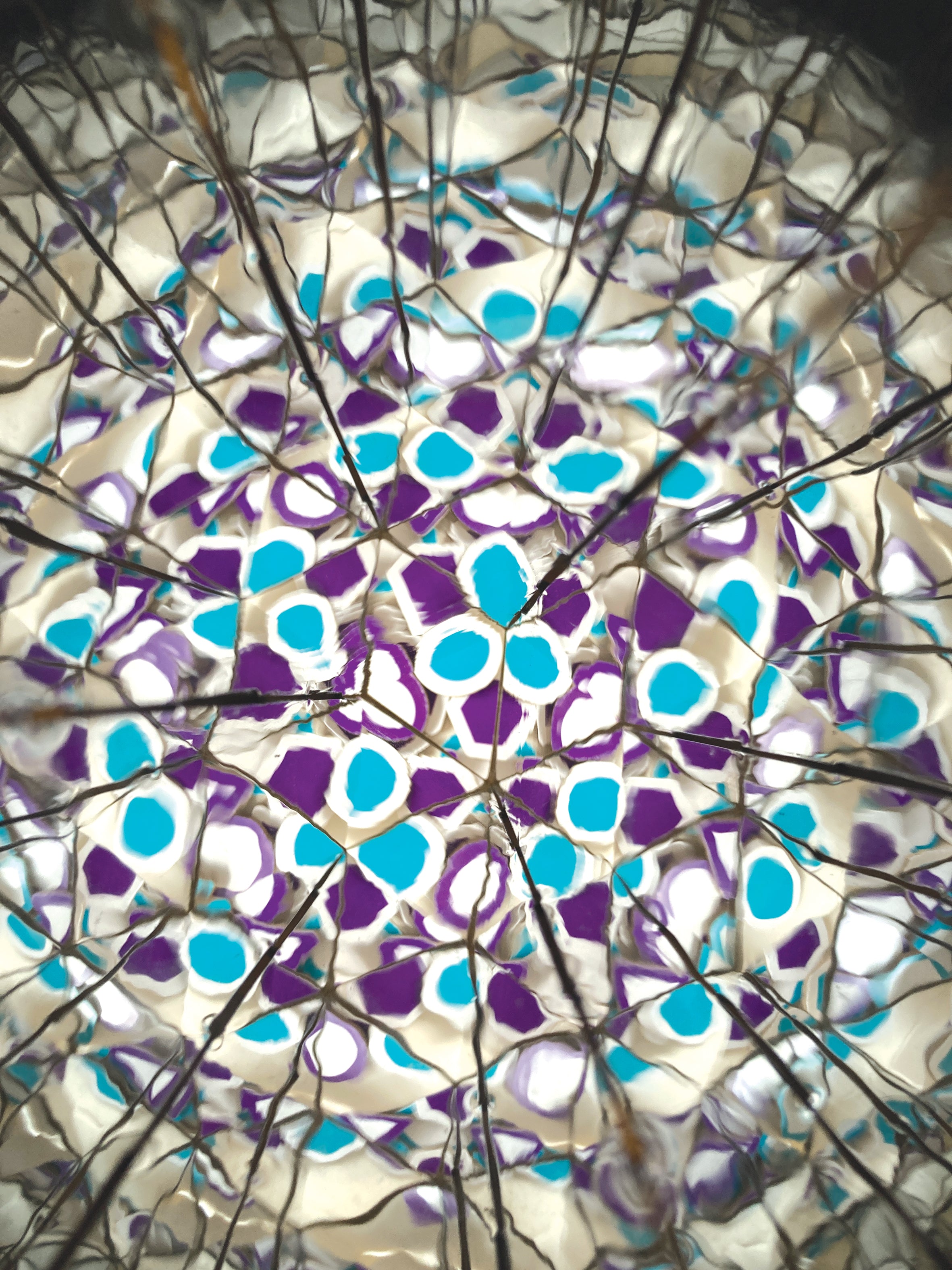 A close-up of a stained glass window design featuring a circular pattern of purple and bright blue shapes set within a white and clear textured glass grid.