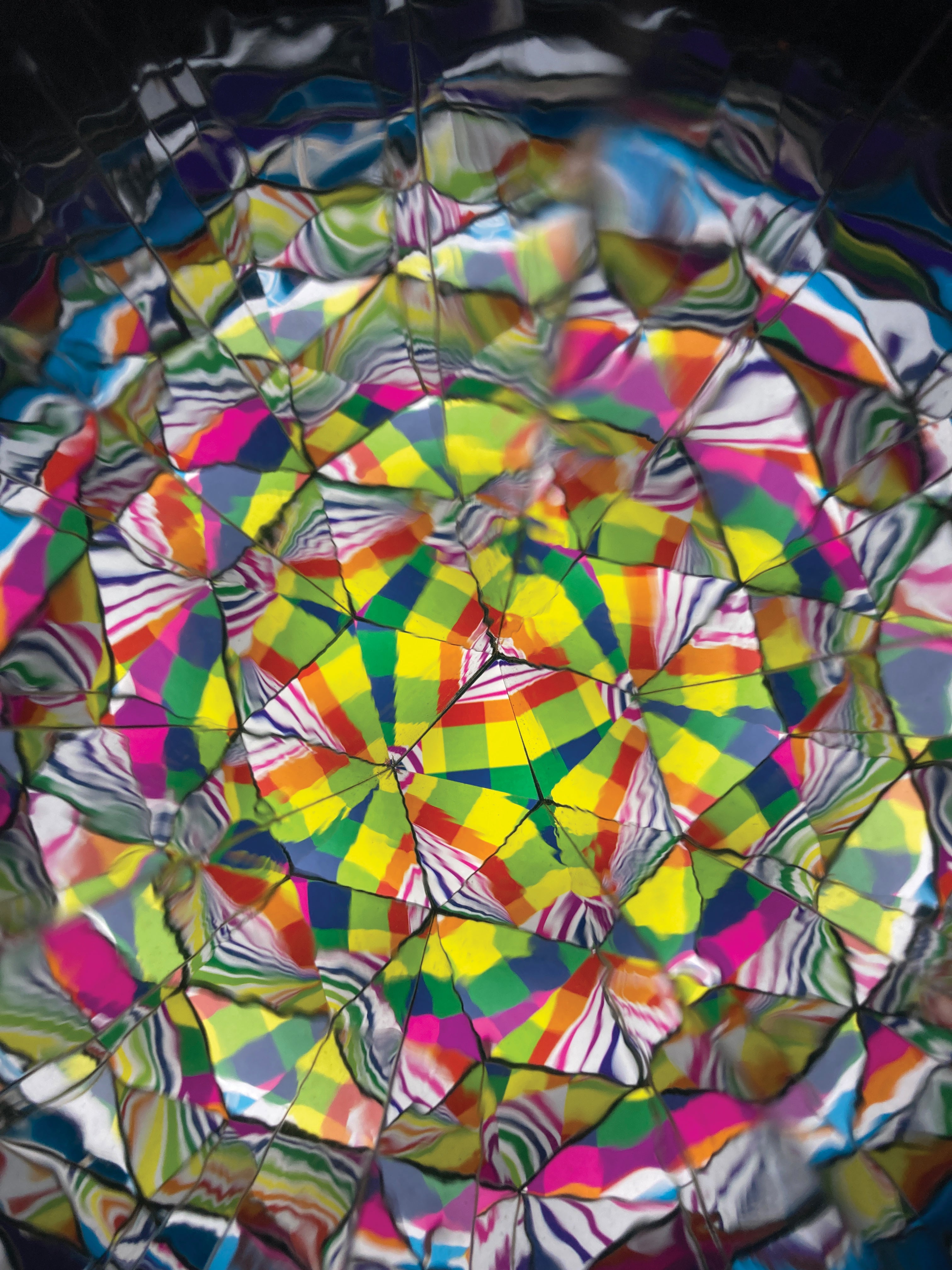 A highly reflective, multicoloured surface with an abstract, kaleidoscopic pattern of geometric facets in yellow, green, pink, blue, orange, and black.
