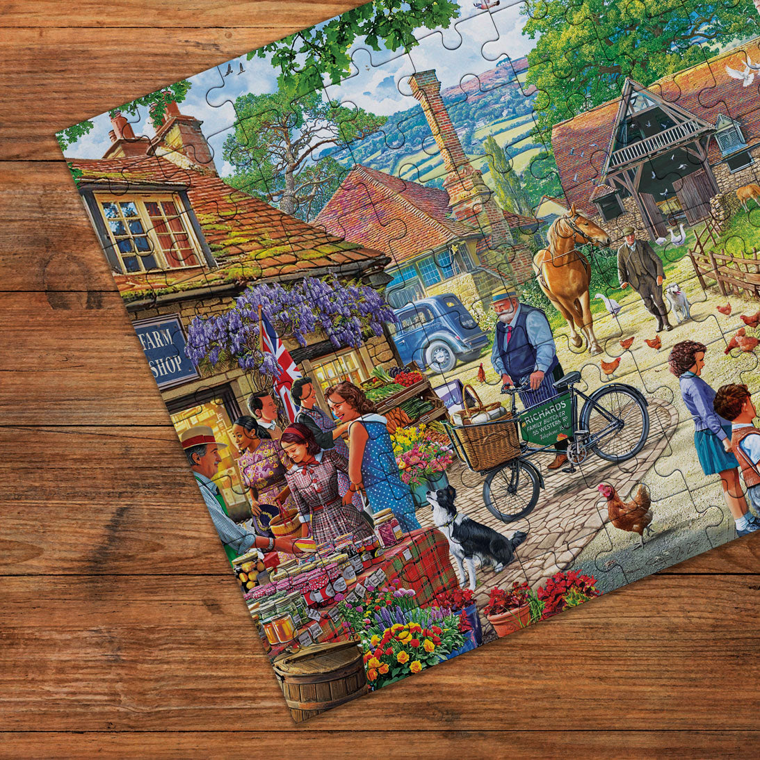 A completed jigsaw puzzle depicting a colourful rural village scene with people, animals, a farm shop, and a blue car, photographed on a wooden tabletop.