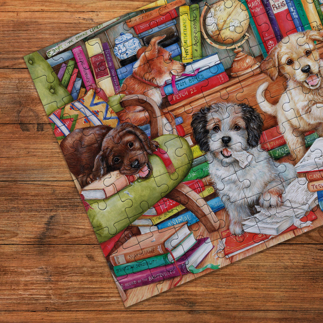 A completed jigsaw puzzle featuring three playful dogs surrounded by books and a globe, placed on a wooden floor. The puzzle pieces are clearly visible, and the artwork is highly detailed with warm, cozy tones.