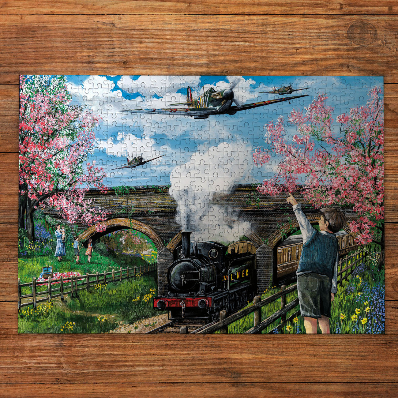 Jigsaw puzzle with a scenic design of a train, people, and cherry blossoms on a wooden surface.