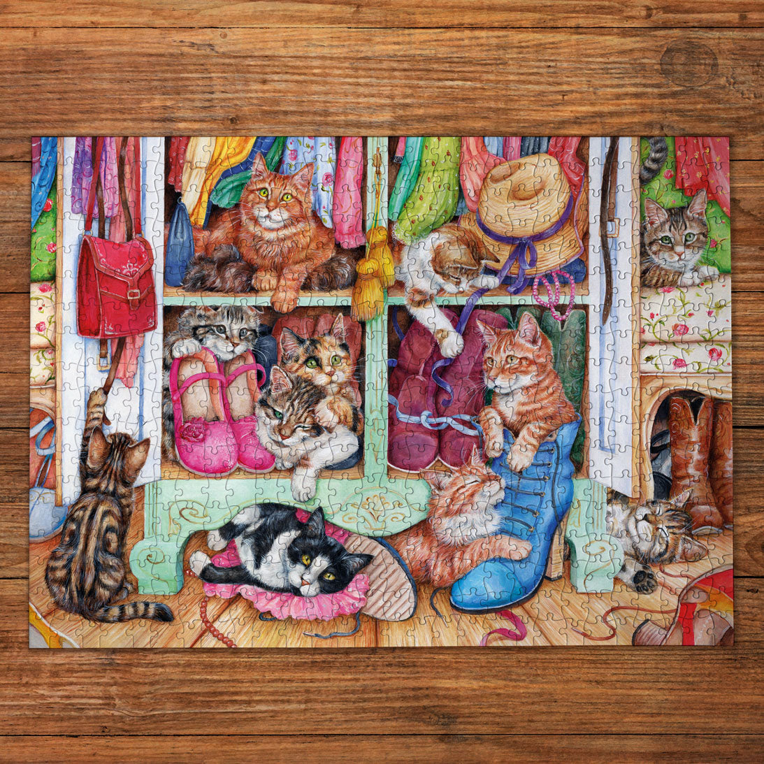 A completed jigsaw puzzle featuring a whimsical illustration of multiple cats in a colorful closet, displayed on a wooden surface. The puzzle design includes orange tabby cats, a black and white cat, pink shoes, a red bag, and various clothing items.