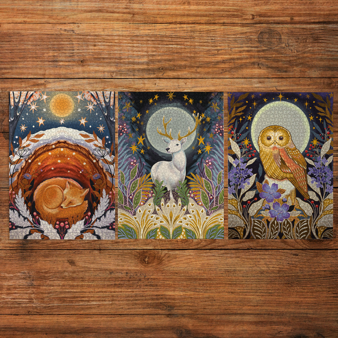 Three vertical art prints with whimsical woodland animal illustrations are arranged side by side on a rustic wooden plank background. The left print shows a sleeping fox in a nest under a starry sky; the center print depicts a white deer under a moonlit sky; the right print features an owl among purple flowers and gold stars.