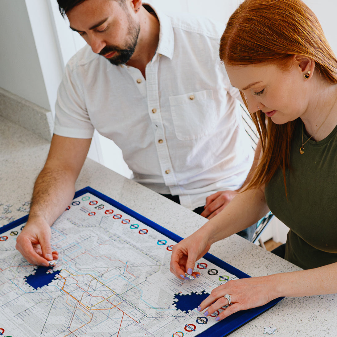 Lifestyle image of Jigsaw puzzle with a map of London's underground system in process of puzzling by woman and man