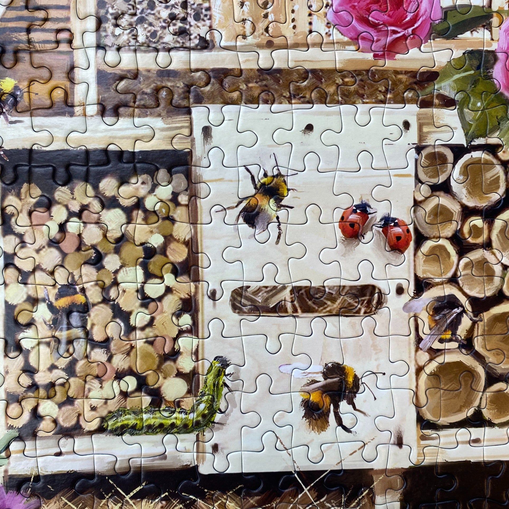 A completed jigsaw puzzle featuring a rustic beehive scene with bees, ladybugs, a caterpillar, honeycomb logs, and flowers on a white wooden board.