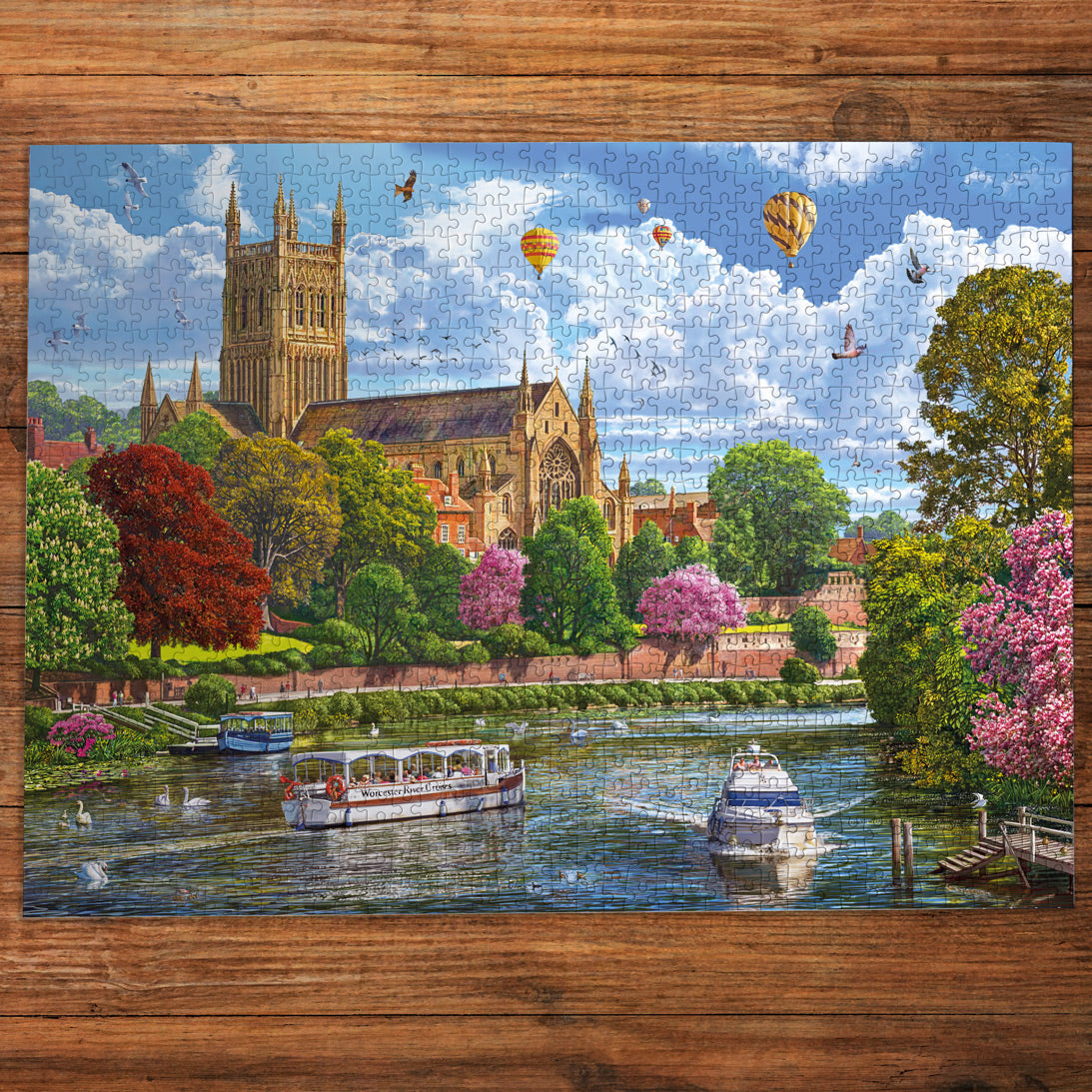 Jigsaw puzzle with a cathedral, boats, and hot air balloons on a wooden frame.