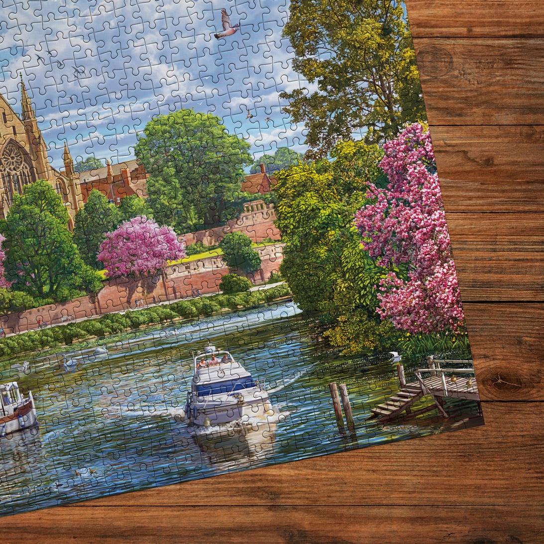 Jigsaw puzzle with a scenic view of a river, boats, and cherry blossom trees on a wooden surface.