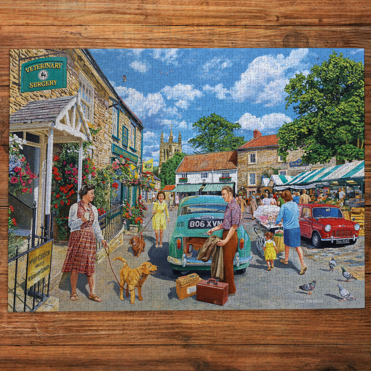 Illustration of a village street scene with people, dogs, and vintage cars on a wooden surface.