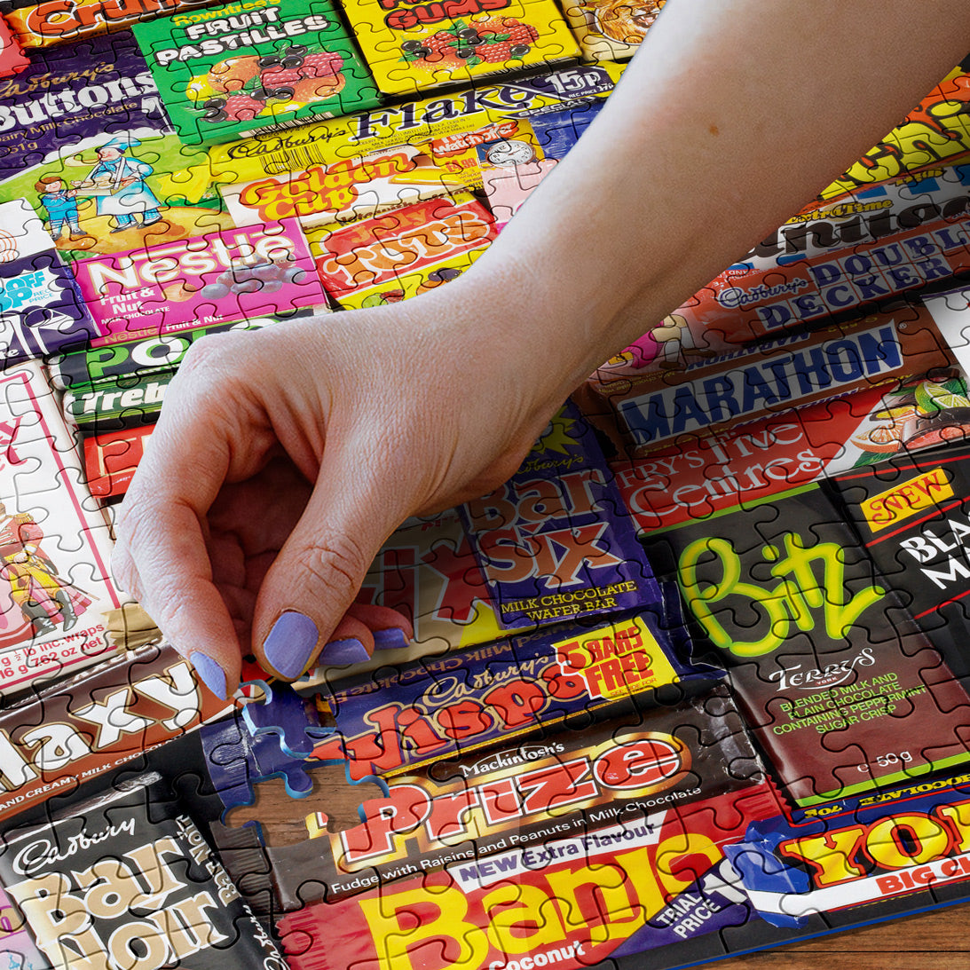 Hand assembling a puzzle with colorful candy bar-themed pieces.