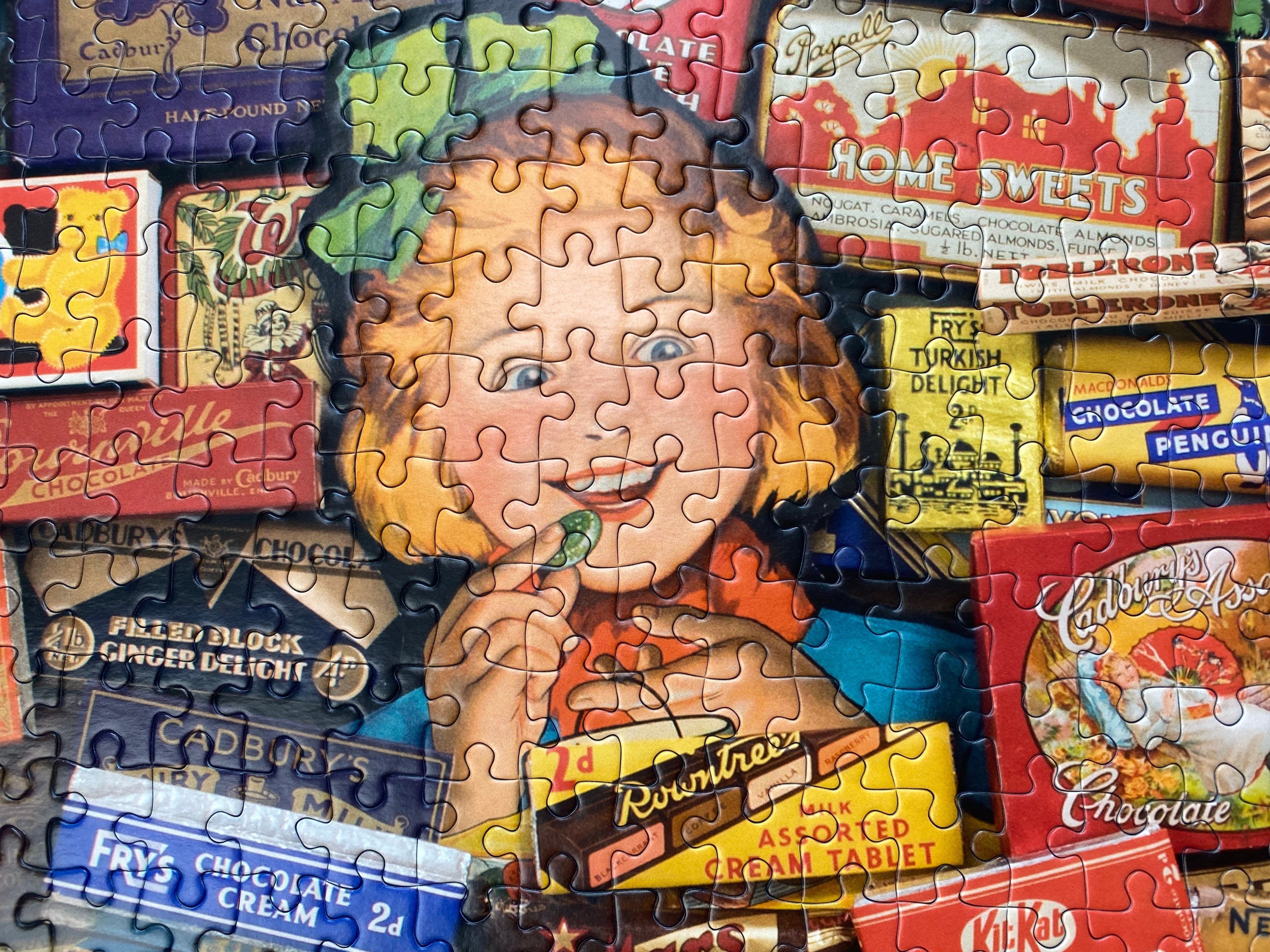A completed jigsaw puzzle showing a vintage-style illustration of a smiling girl with curly hair surrounded by colourful illustrated chocolate and candy boxes, including Cadbury.