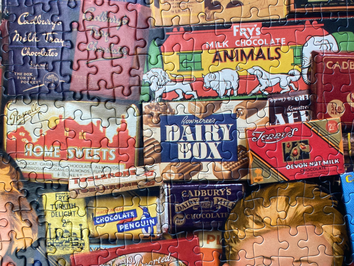 A completed jigsaw puzzle featuring a collage of vintage chocolate advertisements, including Cadbury, Fry's, and America's Dairy Box, with a child's face partially visible in the lower right corner.