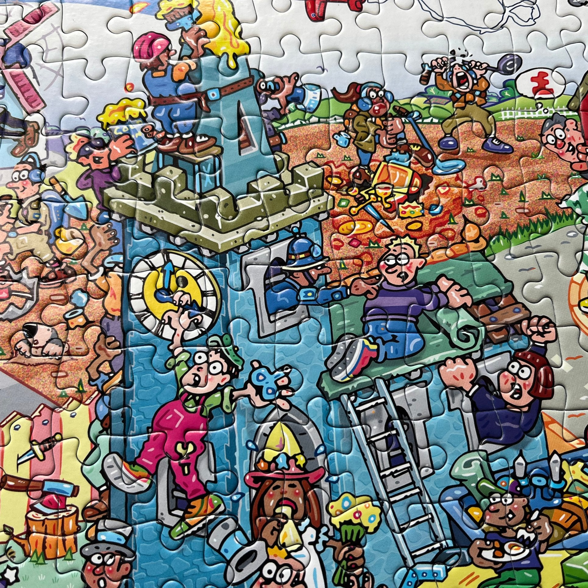 A completed jigsaw puzzle featuring a highly detailed, colourful cartoon scene with many characters, tools, and playful elements, photographed close up with puzzle pieces still visible throughout.
