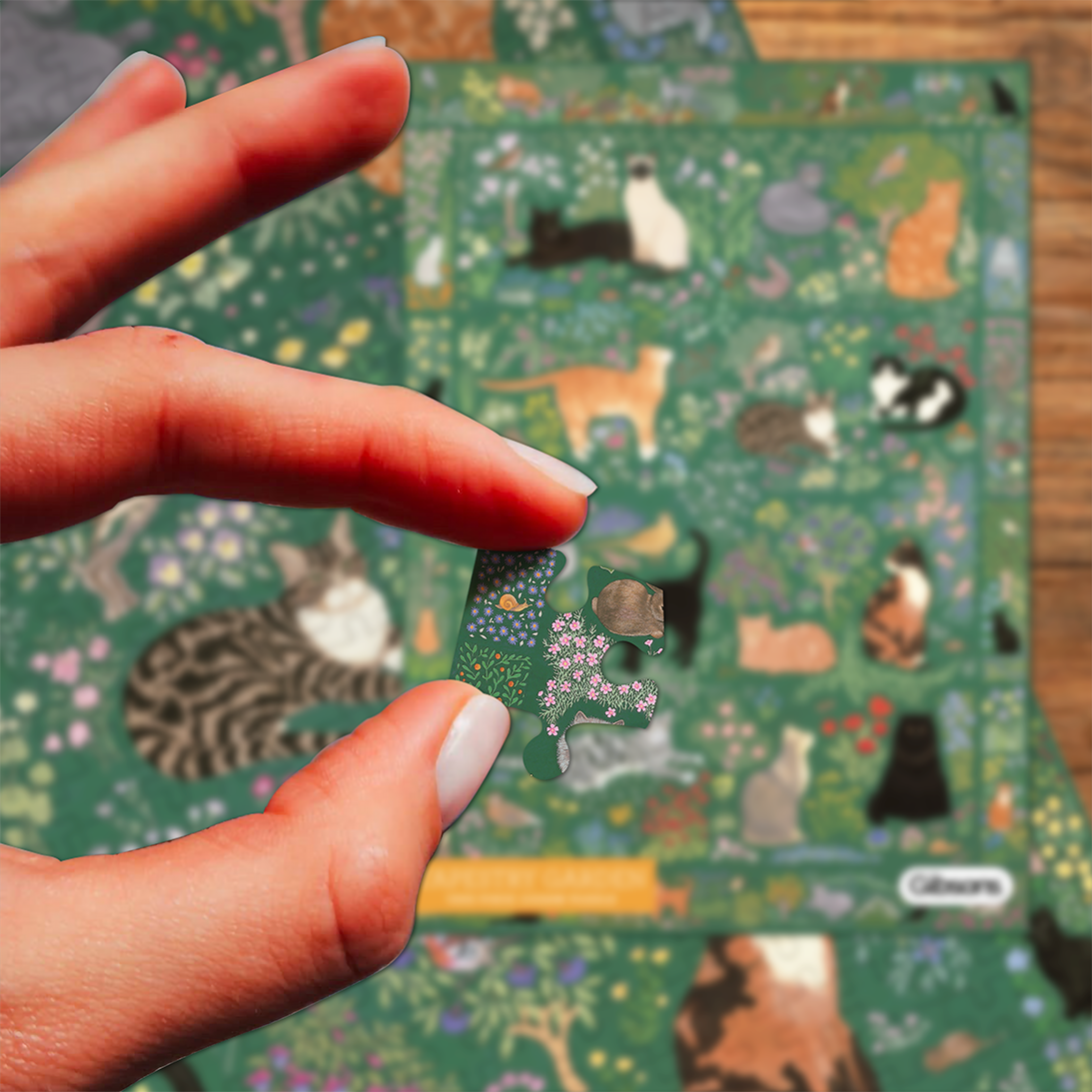 Hand holding a puzzle piece in front of a colorful puzzle with cat illustrations.