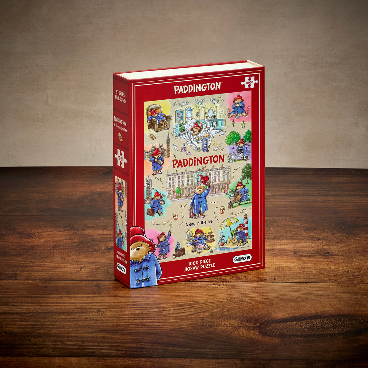 Paddington-themed 1000-piece jigsaw puzzle box standing upright on a wooden tabletop against a neutral textured wall. The box is predominantly red with a colourful illustrated cover showing Paddington.