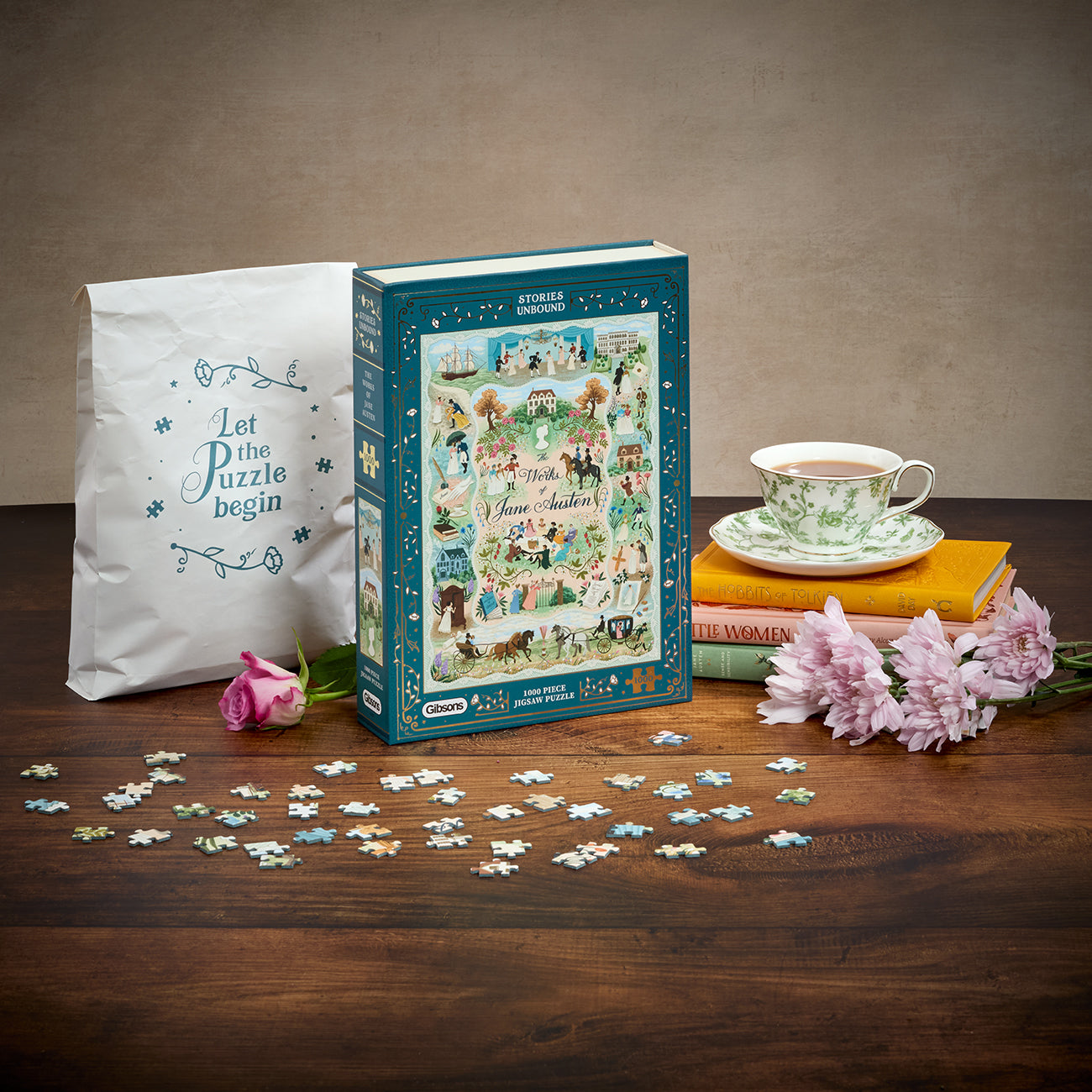 A boxed jigsaw puzzle set displayed on a wooden table with loose puzzle pieces scattered in front. The box is teal and features a colorful illustrated scene.