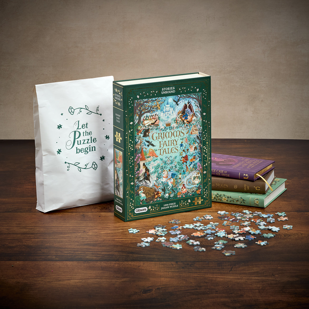 A boxed jigsaw puzzle set titled 'Grimm's Fairy Tales' stands on a wooden table beside a white paper bag that reads 'Let the puzzle begin.' Several loose puzzle pieces are scattered in front, and two decorative books sit behind the box.