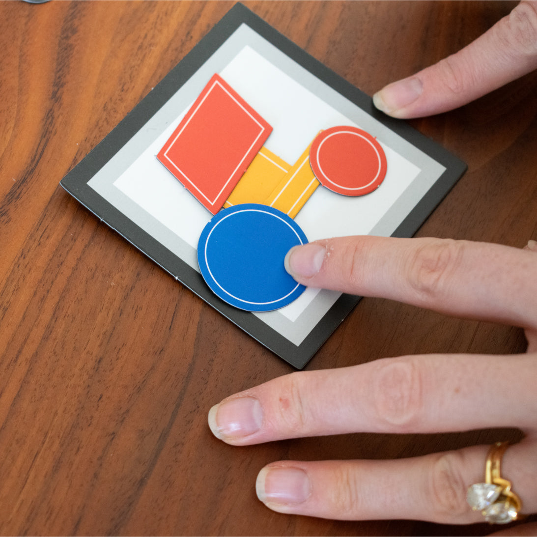 Hand interacting with a small card and magnetic pieces displaying colourful shapes