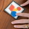 Hand interacting with a small card and magnetic pieces displaying colourful shapes
