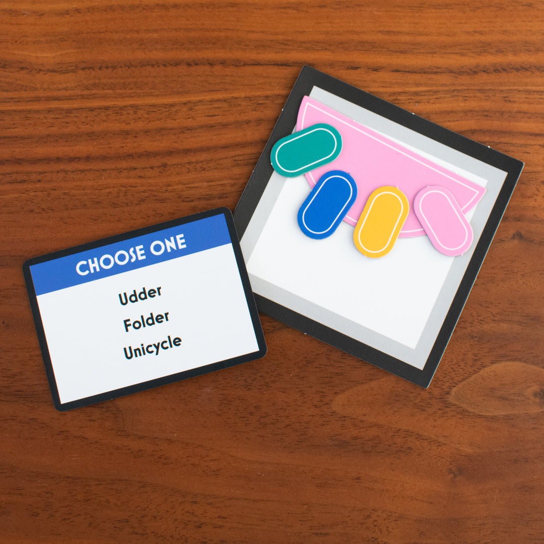 Card game with colorful magnetic shapes and a card labelled 'CHOOSE ONE' on a wooden surface