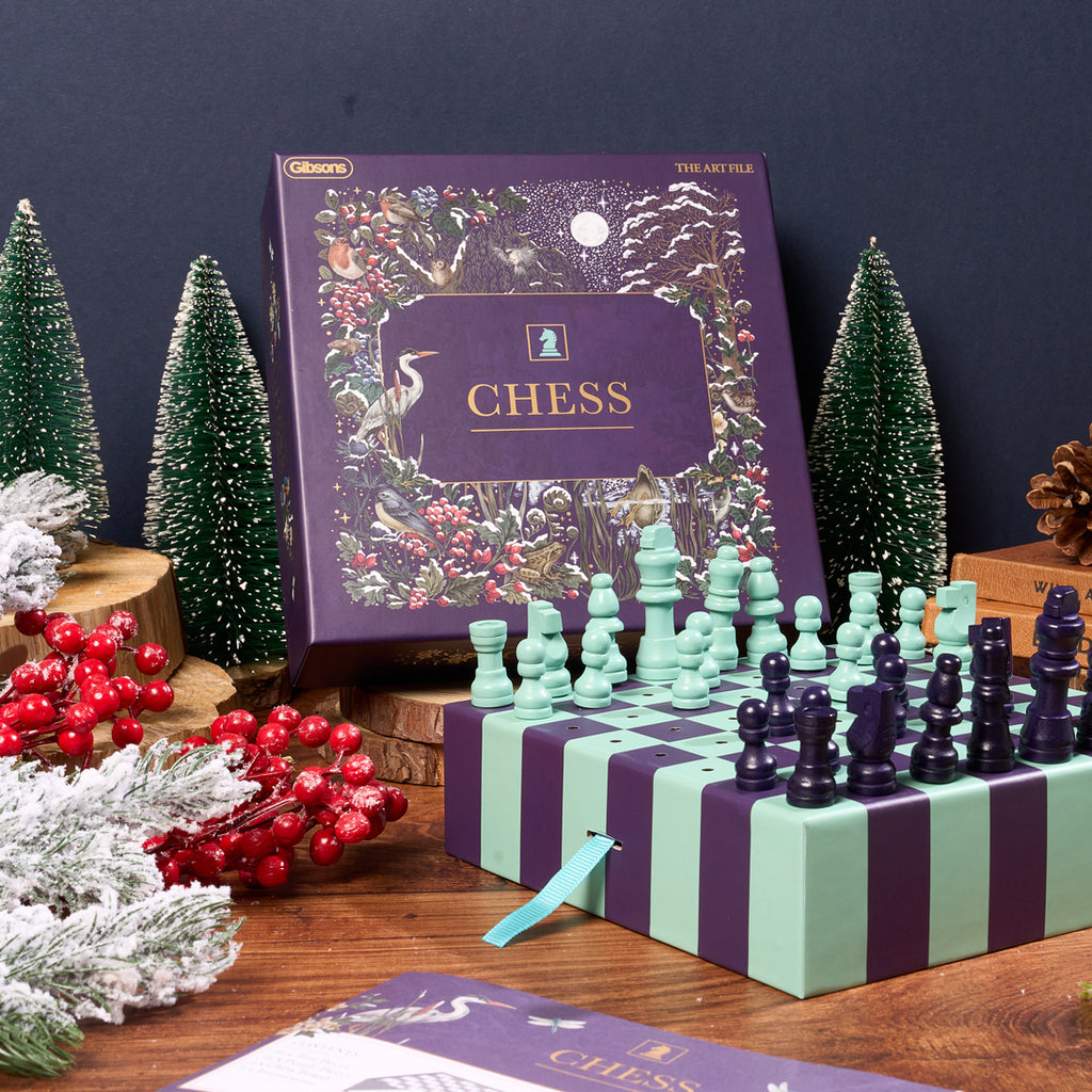Chess set with decorative packaging on a wooden surface with Christmas trees and berries.