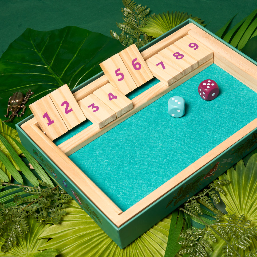 Board game with numbered tiles and dice on a green surface with leaves