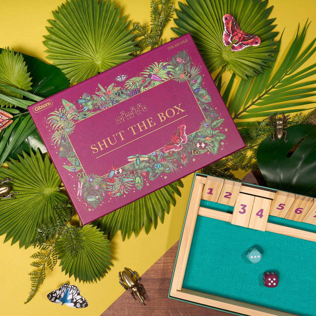 Shut the Box game set with decorative box on a yellow background with green leaves.