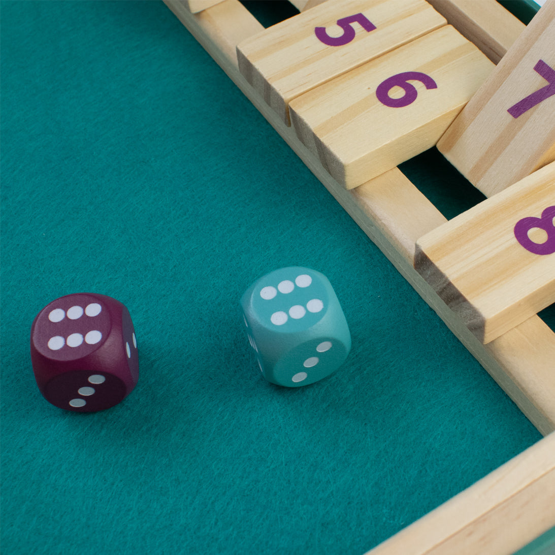 Two dice on a green surface next to a wooden game board with numbers.