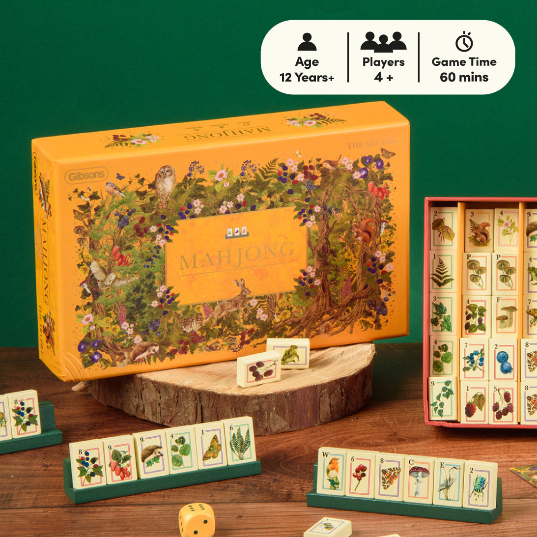 Gibson's Mahjong game set displayed on a wooden surface against a dark green background, with the orange illustrated box, tiles, dice, and a side rack of cards. A white badge at the top shows age 12+, players 4+, and game time 60 mins.