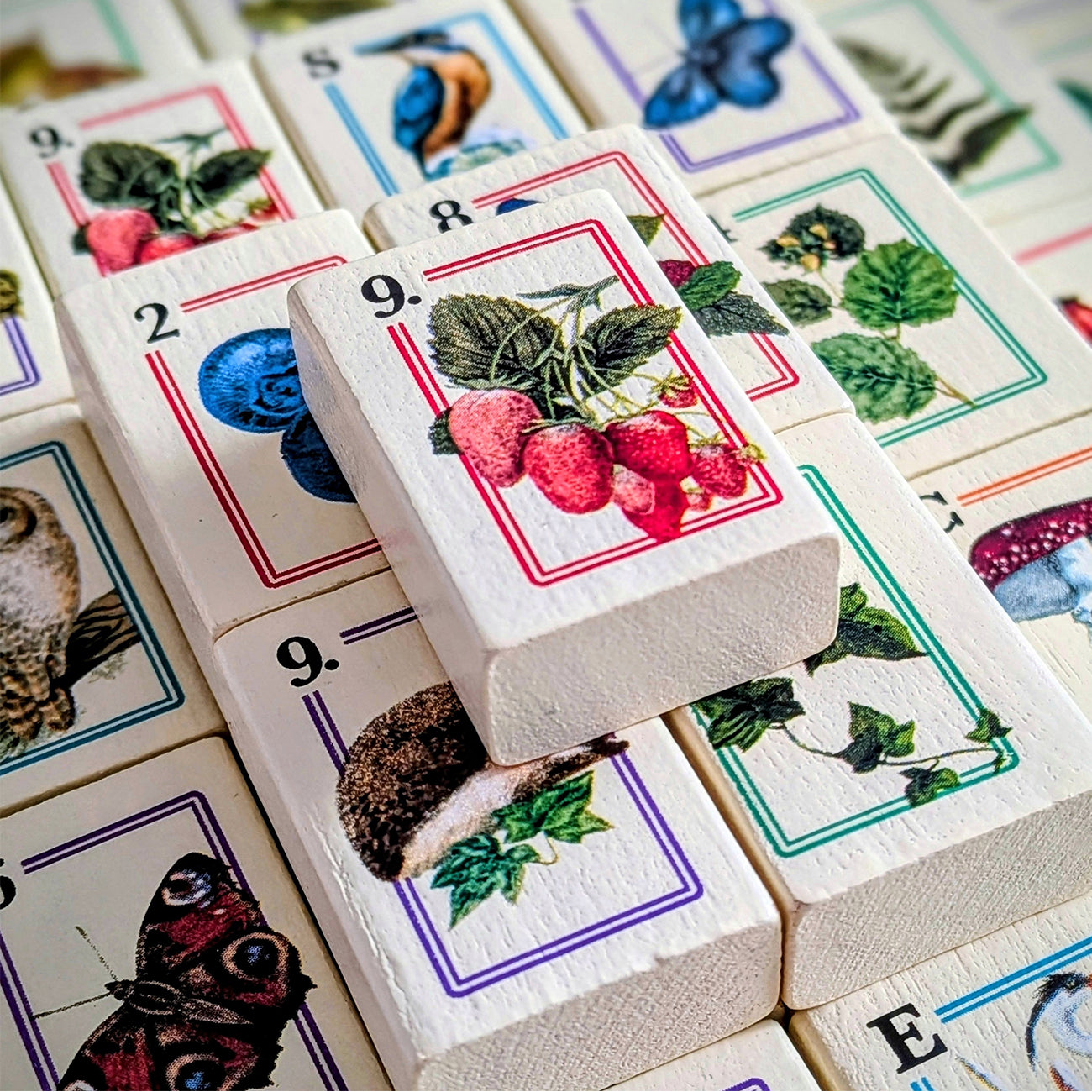 Wooden Mahjong tiles featuring illustrated nature and animal designs, including strawberries, blueberries, a butterfly, an owl, and a mushroom, arranged in a close-up stack.