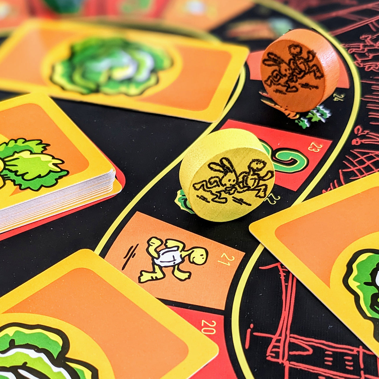 Close-up of a colourful card game setup with illustrated cards, two wooden dice, and a black game board featuring curved yellow and red tracks.