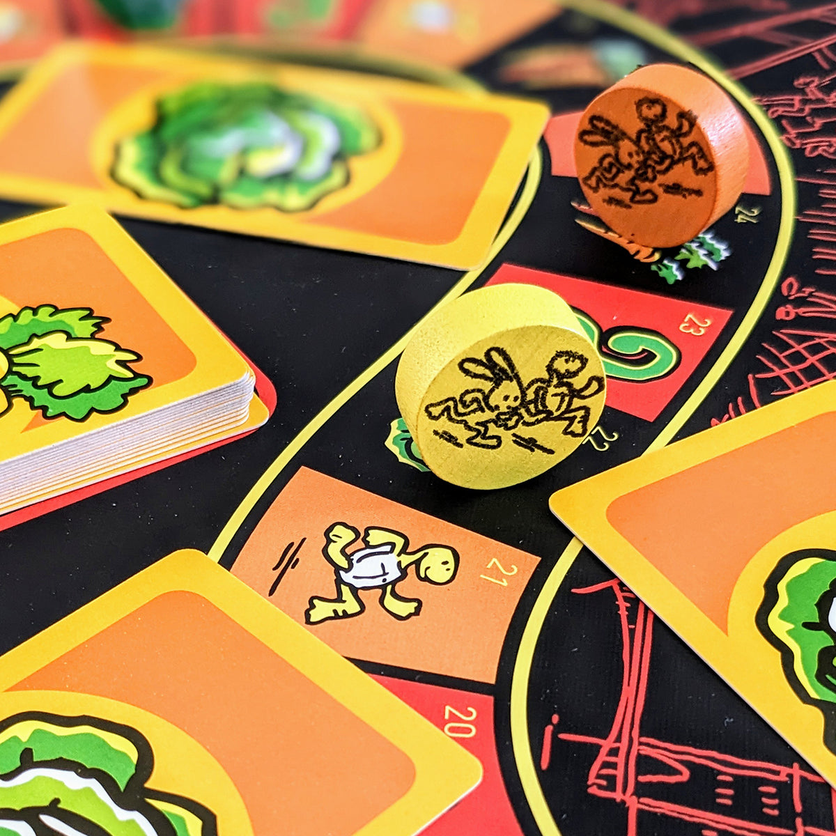 Close-up of a colourful card game setup with illustrated cards, two wooden dice, and a black game board featuring curved yellow and red tracks.