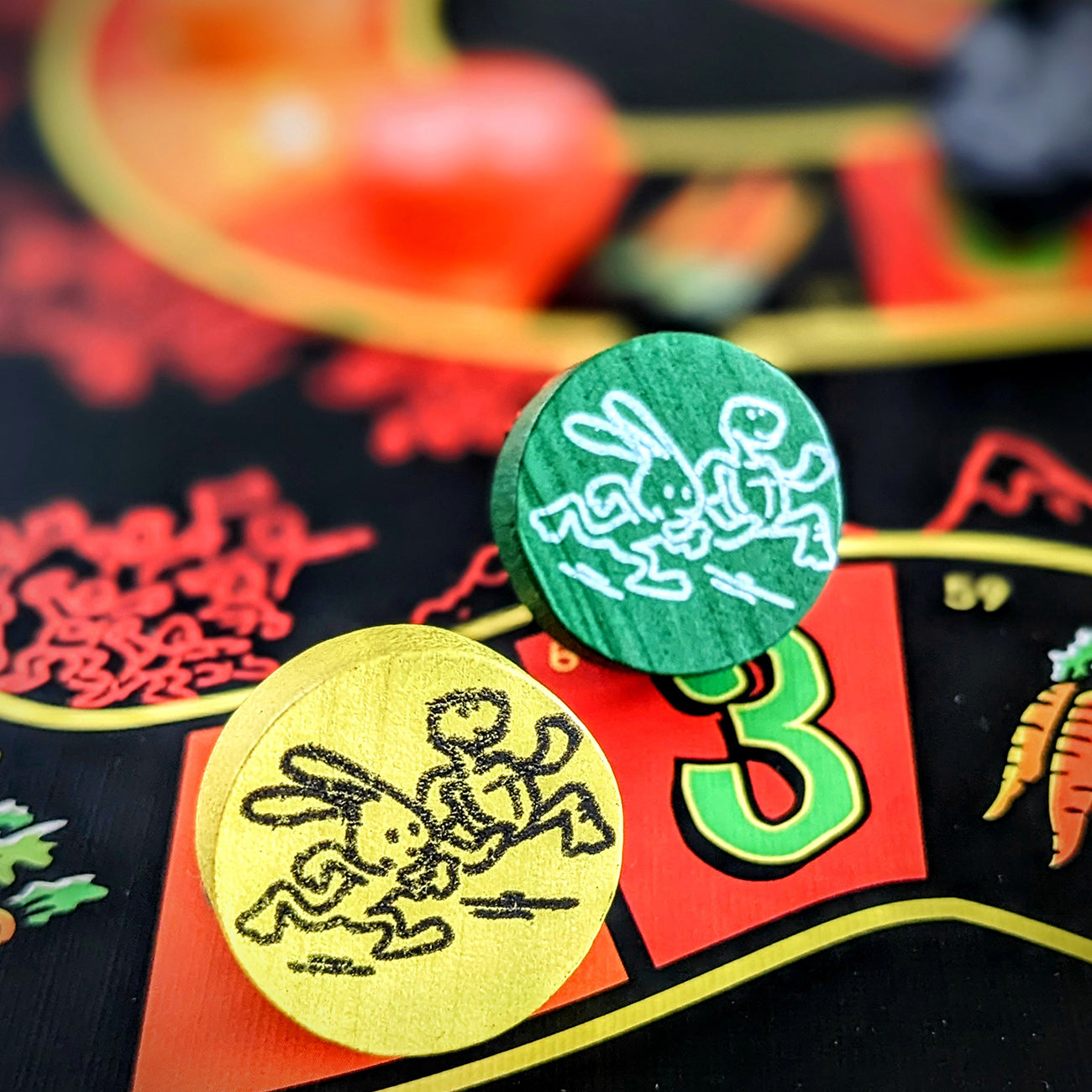 Two round wooden game tokens with rabbit illustrations, one green and one yellow, resting on a colorful board game.
