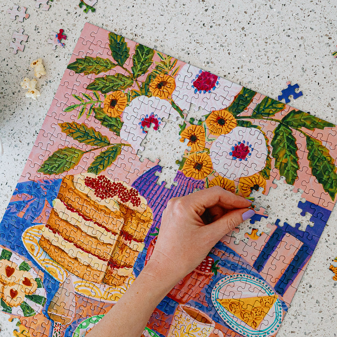 Colorful puzzle with a cake and floral design, hand placing a piece.