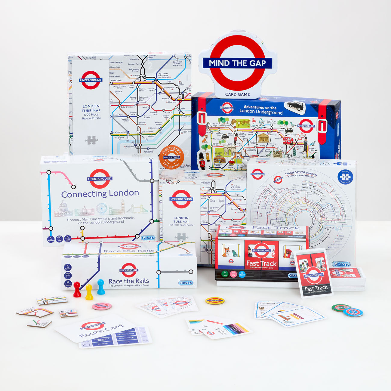 London Underground-themed board game set displayed on a white background, including multiple boxes, cards, tokens, and game pieces. Visible branding includes 'MIND THE GAP' on the sign and 'London Underground' on the packaging.