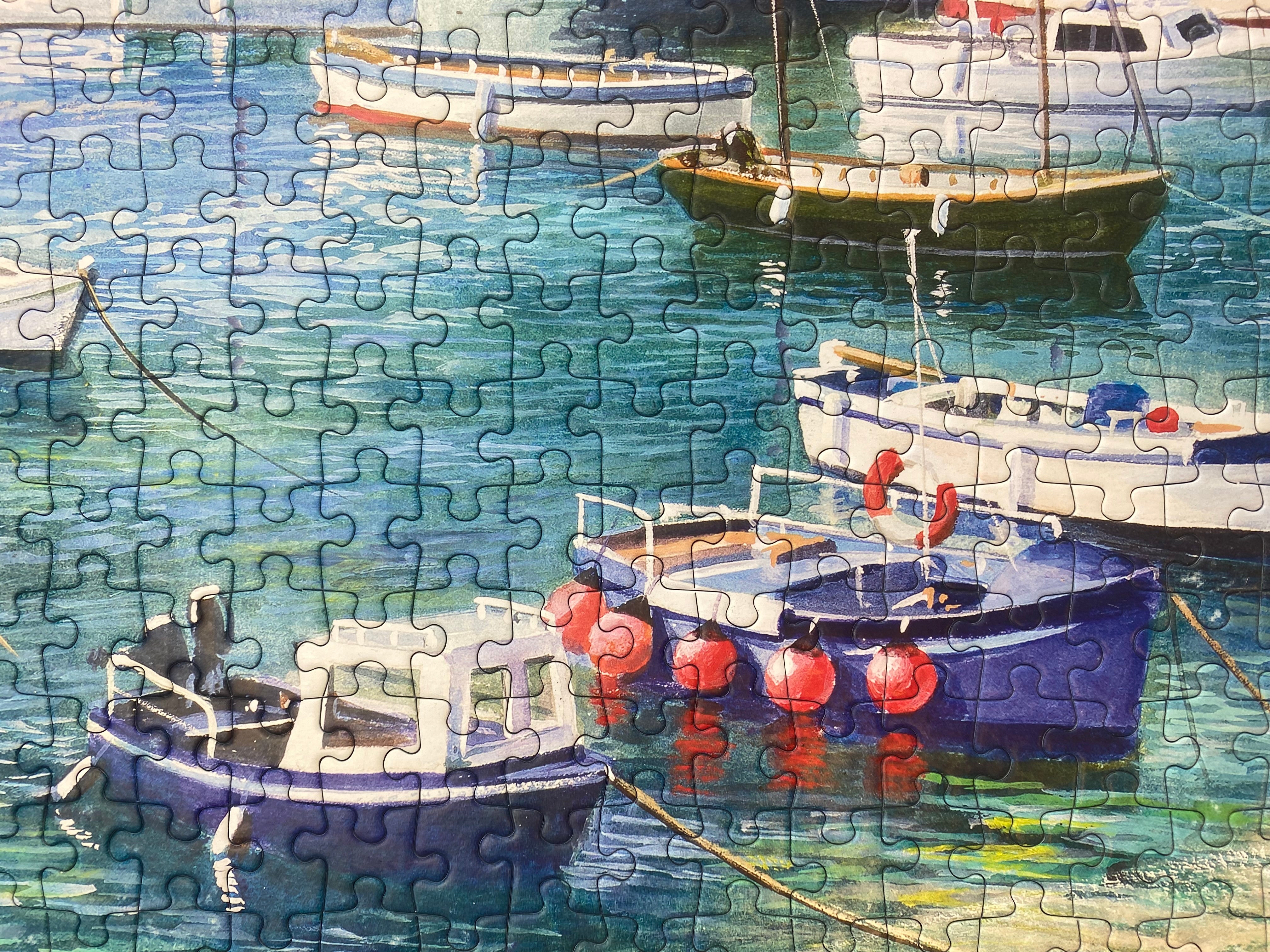 A completed jigsaw puzzle showing a painted harbor scene with several small boats on blue-green water. The puzzle pieces are clearly visible across the entire surface.