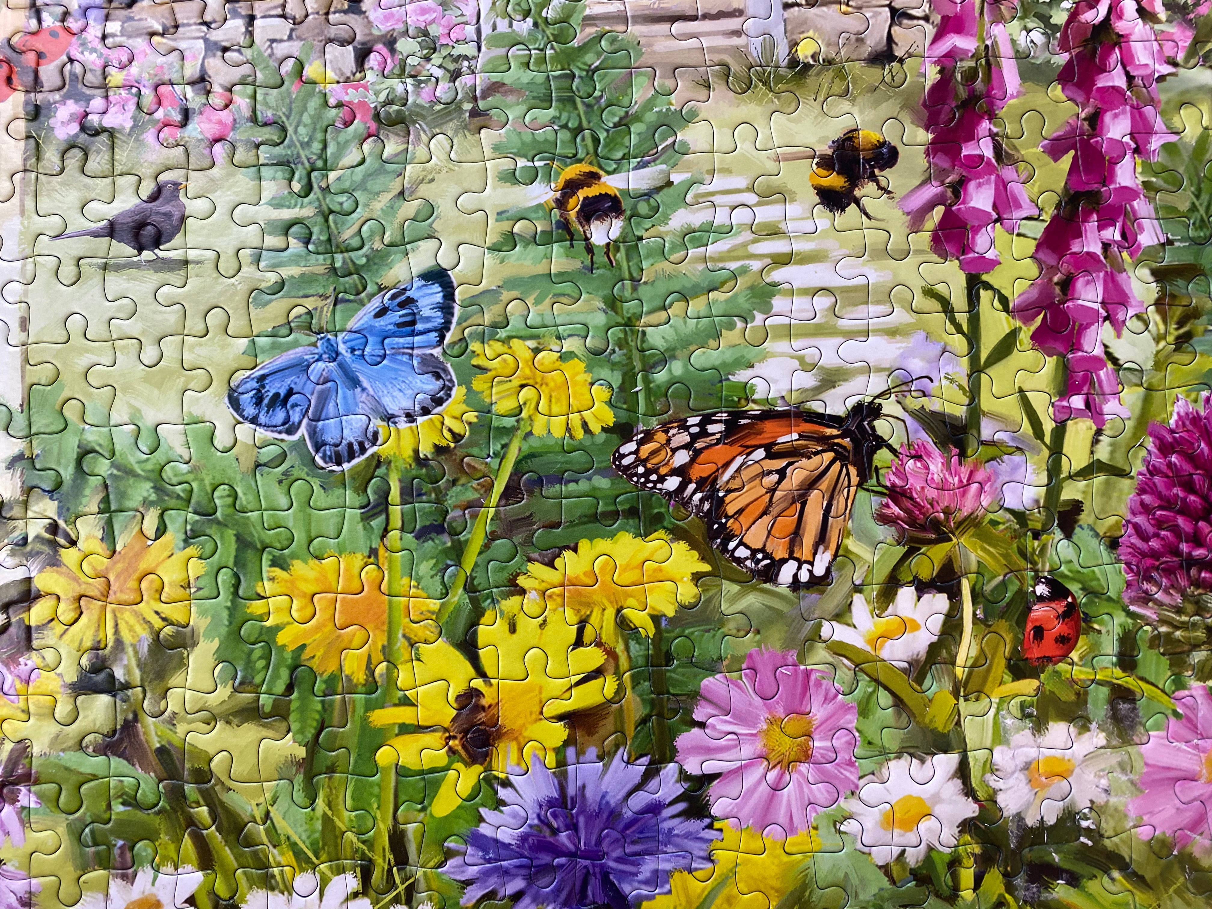 A completed jigsaw puzzle showing a colourful wildflower meadow with a blue butterfly, an orange-and-black monarch butterfly, bumblebees, a ladybug, and birds.