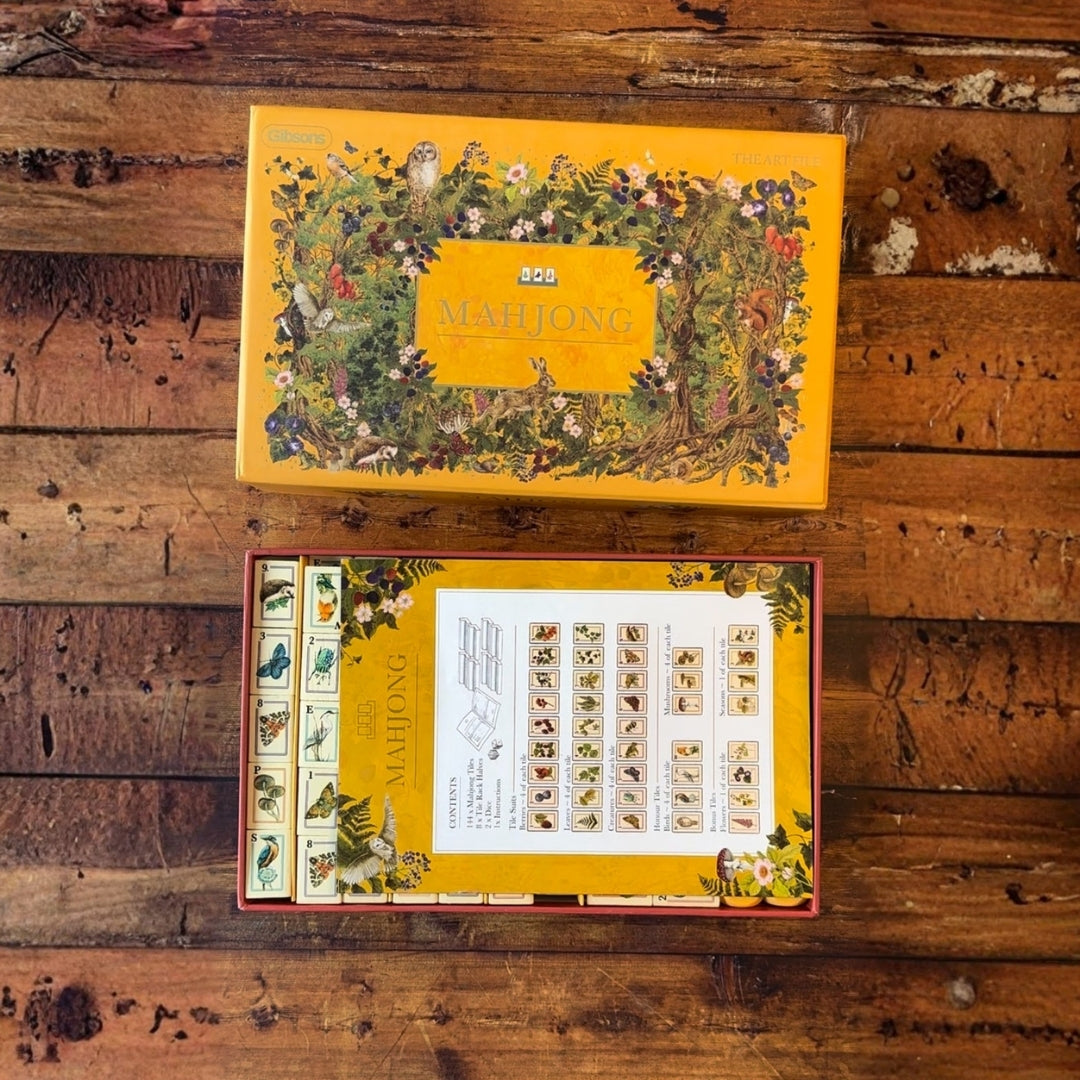 A yellow illustrated box labeled MAHUONG sits on a rustic wooden surface above an open matching box showing printed sheets with small drawings and text.