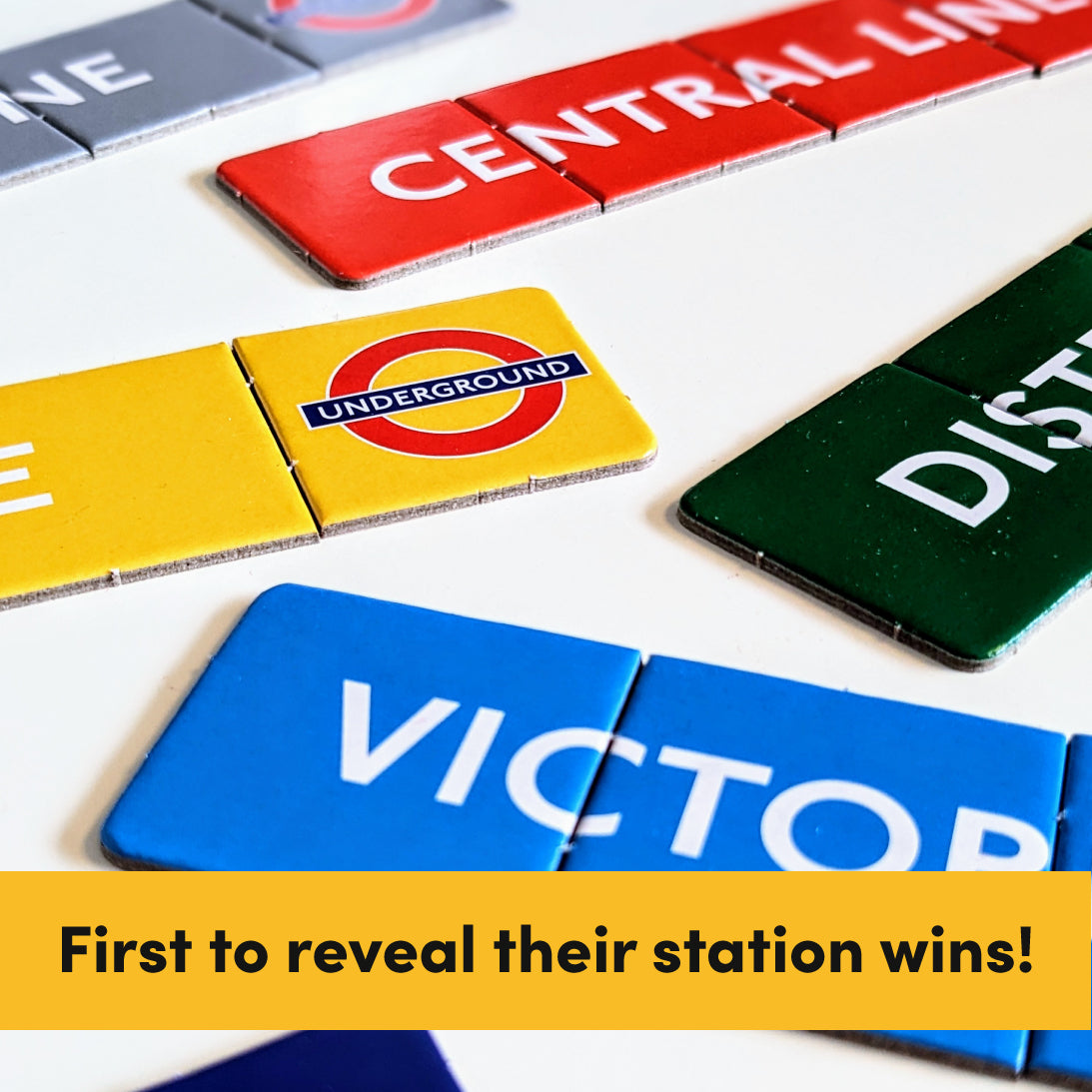 A close-up of colourful London Underground station tile pieces on a white surface, including red Central Line, yellow Underground, green District, and blue Victoria, with a yellow text banner at the bottom reading 'First to reveal their station wins!'.