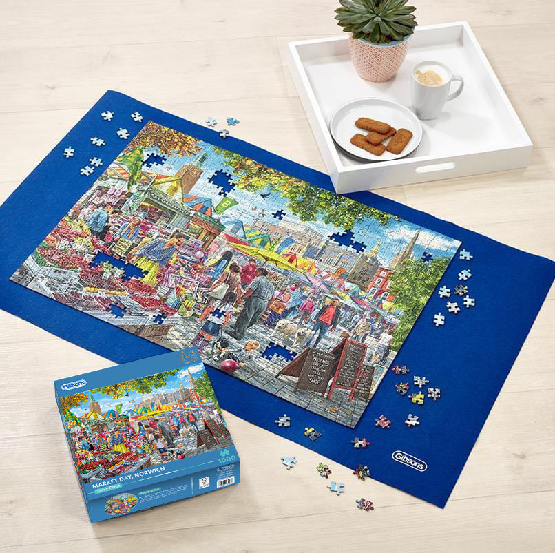 Jigsaw puzzle with completed pieces on a blue mat, partially completed puzzle, and packaging on a wooden surface.